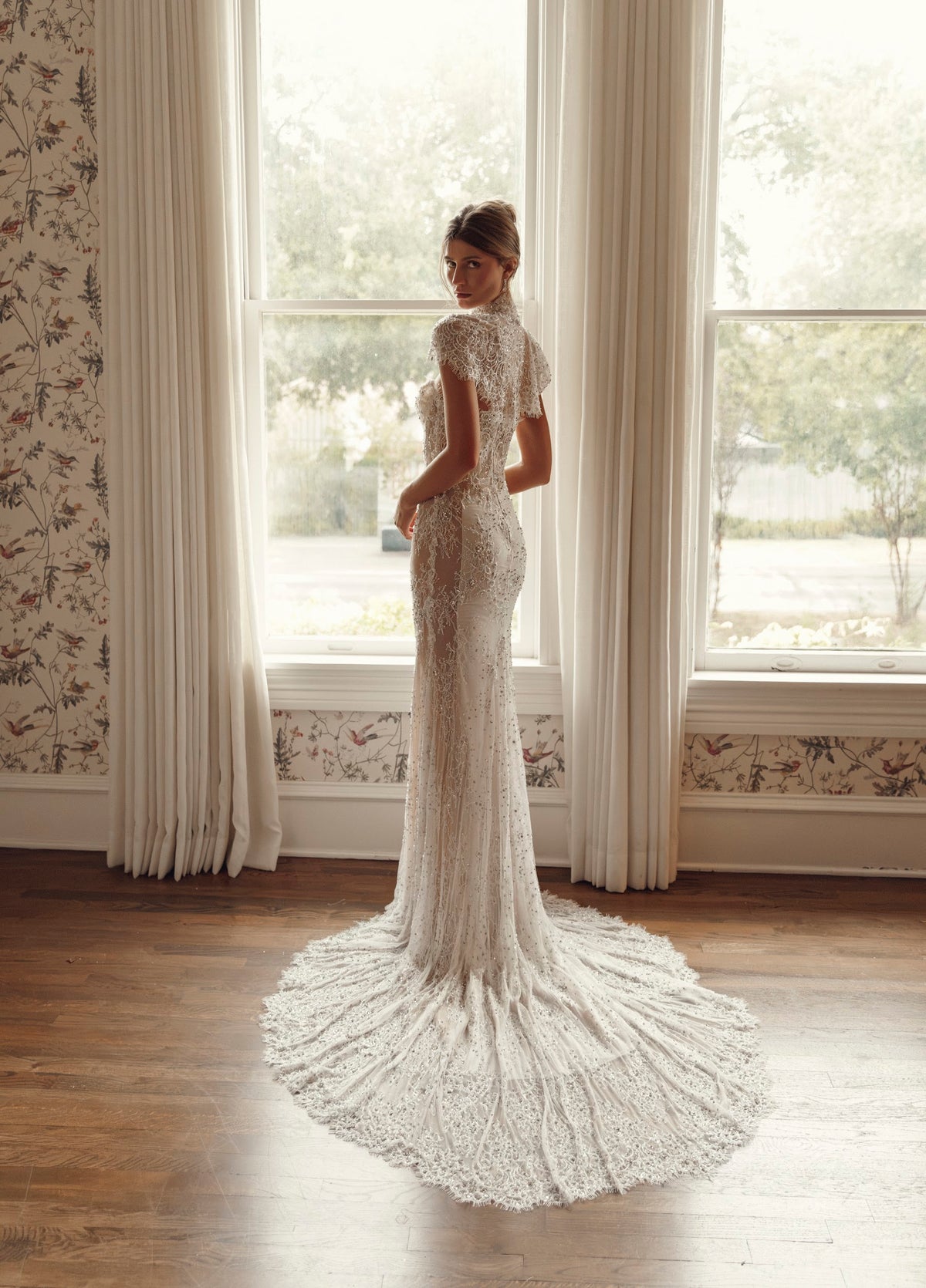 Back view of Julie Vino Noelle 3209 fitted wedding dress with intricate lace embellishment, a rounded sweeping train and a short lace capelet.