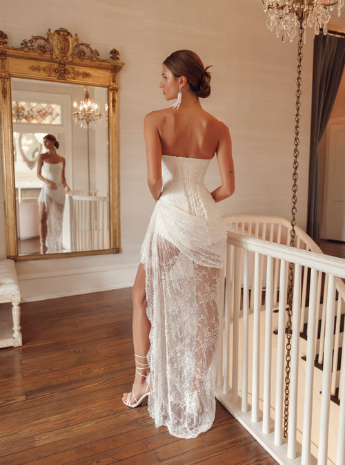 Back view of Julie Vino Yasmin 3212 wedding dress showing an elongated lace-up corset, gathered hip draping and a sheer floral lace skirt.