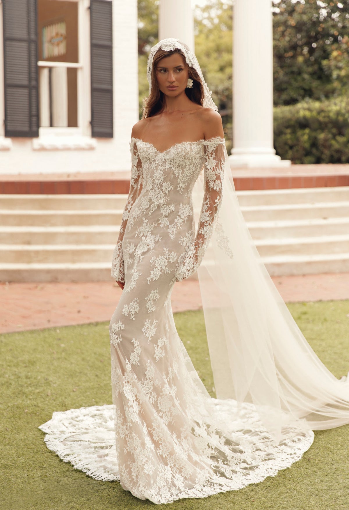 Front view of Mimosa by Julie Vino Petra MB27-23 fitted floral lace wedding dress with an off-shoulder sweetheart neckline and long illusion sleeves.