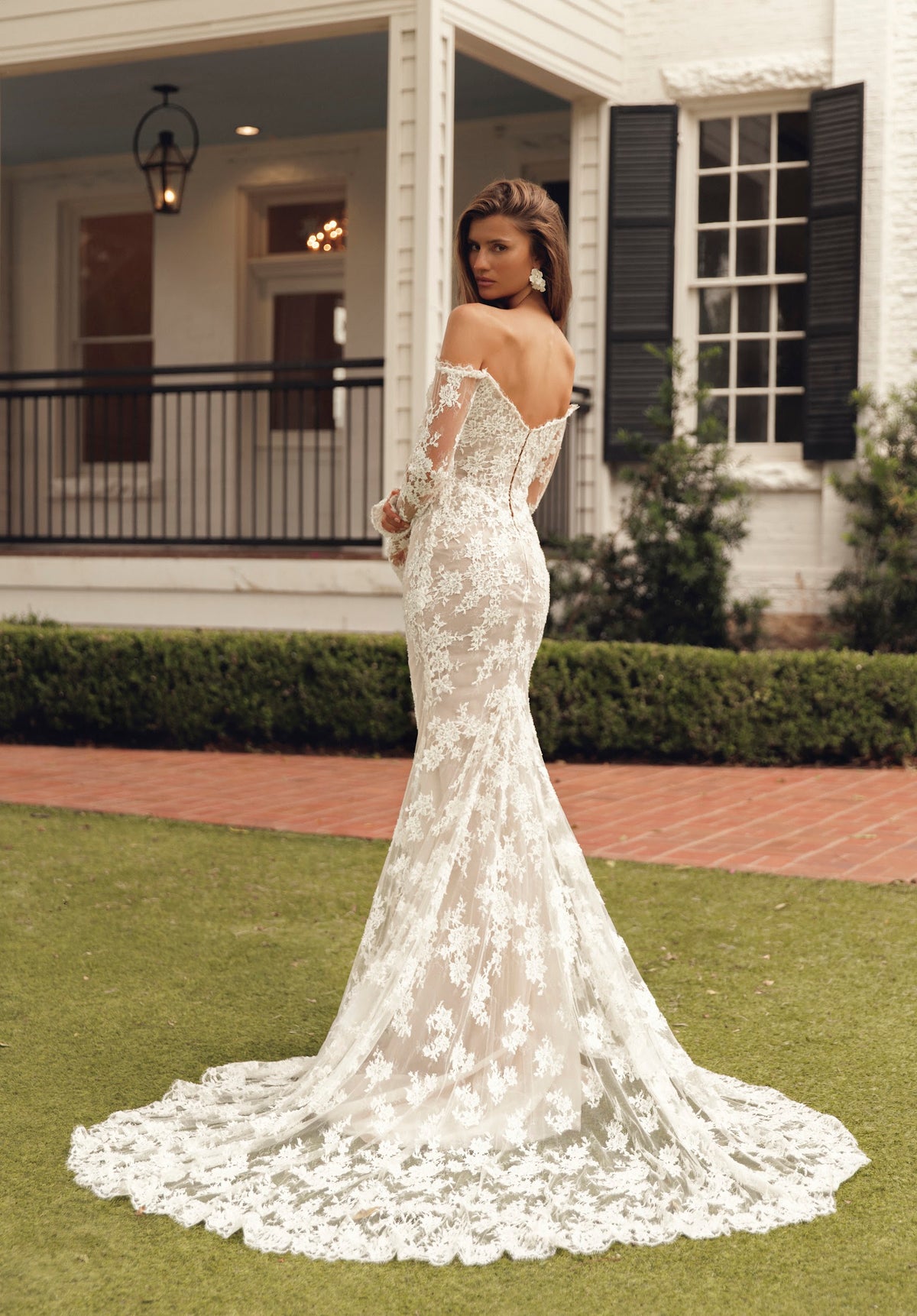Side-back view of Mimosa by Julie Vino Petra MB27-23 lace wedding dress with long sleeves and a scalloped train, styled with a lace-edged veil.