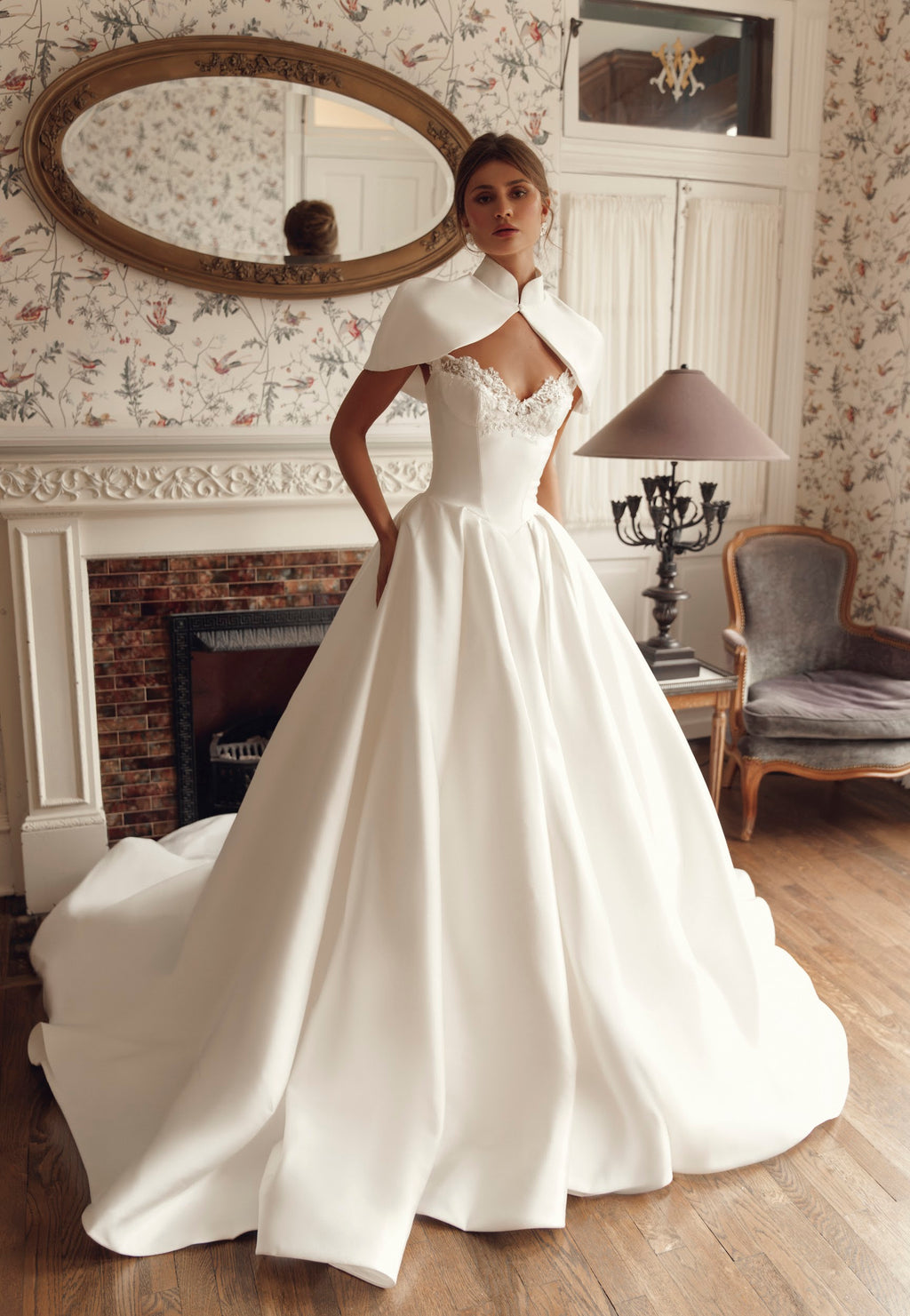 Front view of Mirella PR27-25 by Pure by Julie Vino, showing the lace sweetheart neckline and full pleated skirt, styled with a short bridal cape.