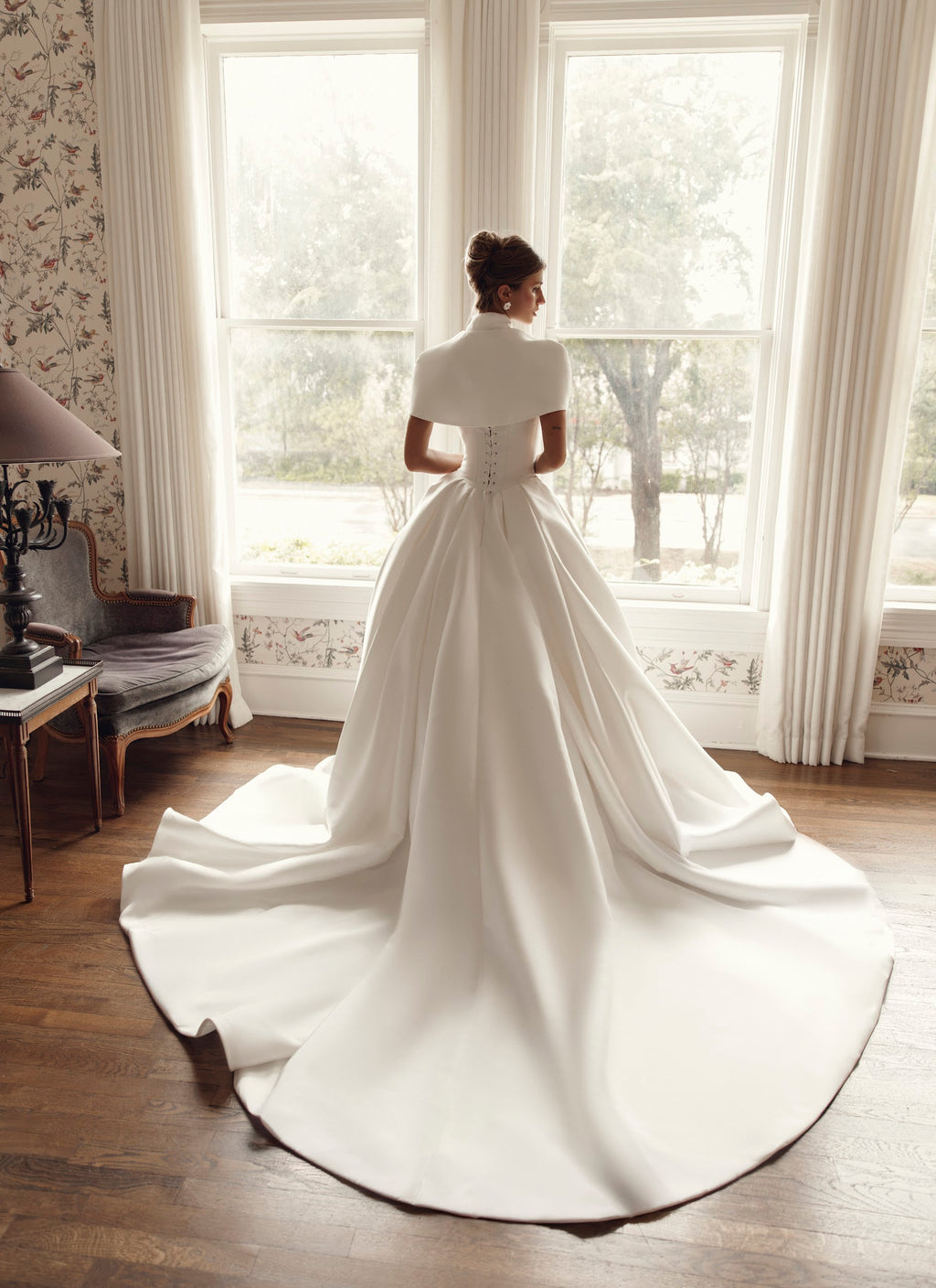 Back view of Mirella PR27-25 by Pure by Julie Vino, showing corset lacing, a full ball gown skirt and sweeping train beneath a structured cape.