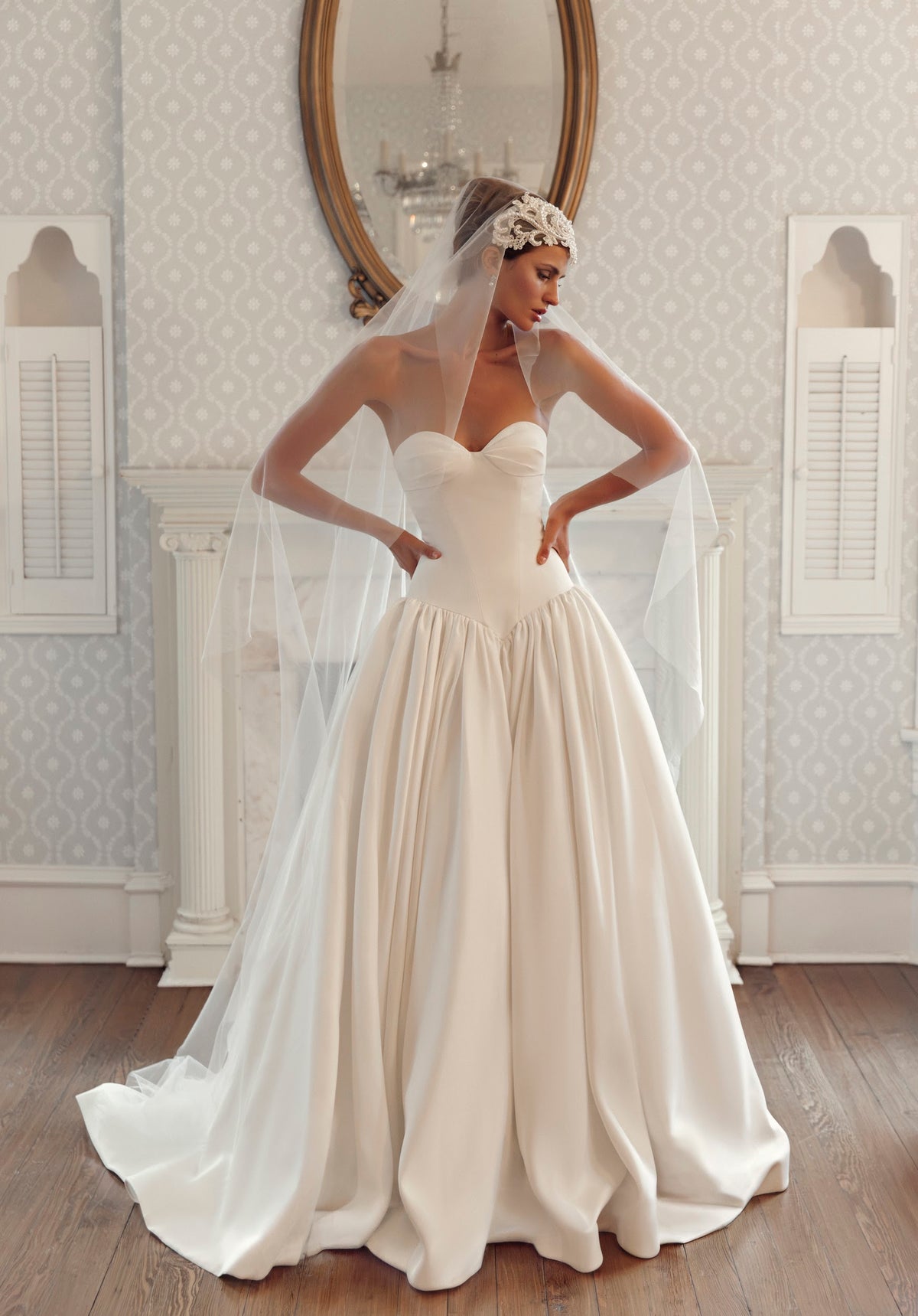 Front view of Fiorelle PR27-27 by Pure by Julie Vino, showing the pleated sweetheart neckline, pointed basque waist and full skirt, styled with a veil.